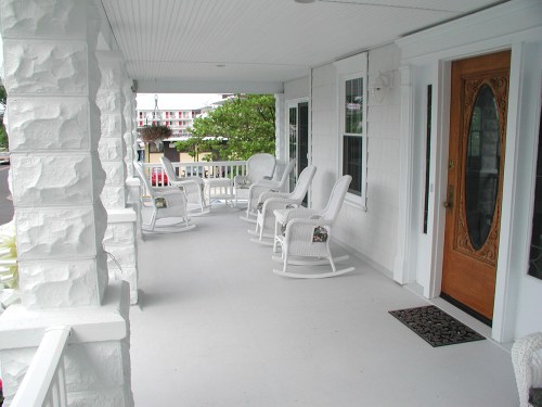 A porch with white rocking chairs and a wooden front door, surrounded by a peaceful outdoor setting.