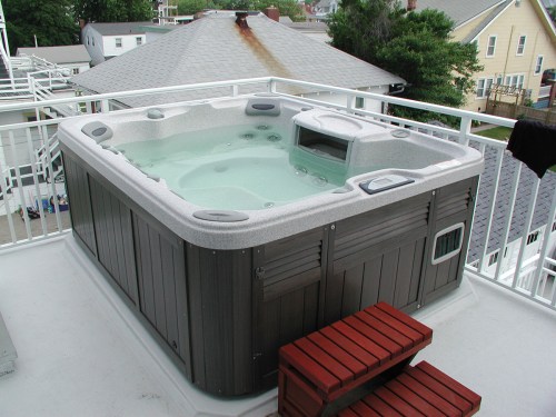 A hot tub on a rooftop terrace, surrounded by buildings and greenery, with steps leading up to it.