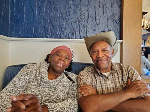 A smiling couple sits together in a cozy restaurant, dressed casually and enjoying each other's company.