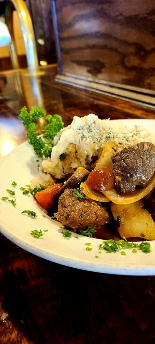 A plate of hearty beef stew with vegetables, served with mashed potatoes and garnished with parsley.