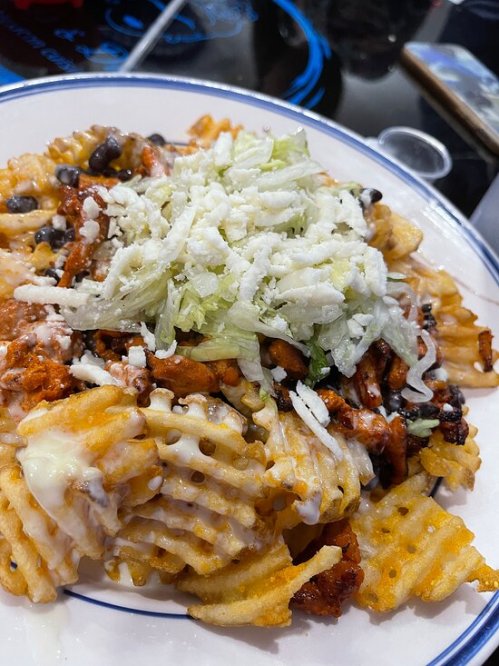 A plate of loaded waffle fries topped with shredded lettuce, cheese, black beans, and seasoned chicken.