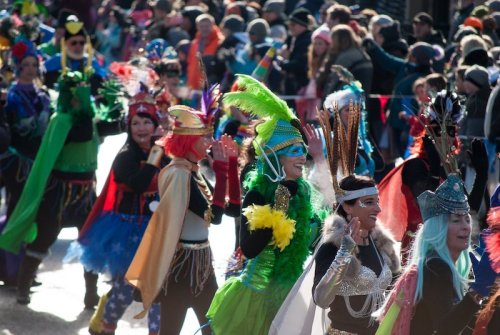 A vibrant parade scene with participants in colorful costumes and feathered headdresses, celebrating joyfully.