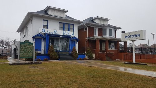 Exterior view of the Motown Museum in Hitsville, USA, featuring a blue and white house and a sign. Grass in the foreground.