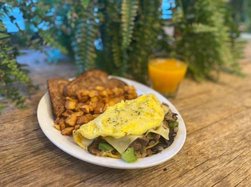 A plate of omelette with vegetables, hash browns, toast, and a glass of orange juice on a wooden table.