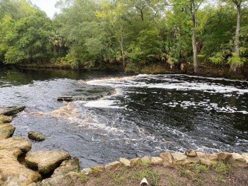 A serene river scene with gentle rapids, surrounded by lush greenery and rocky banks.