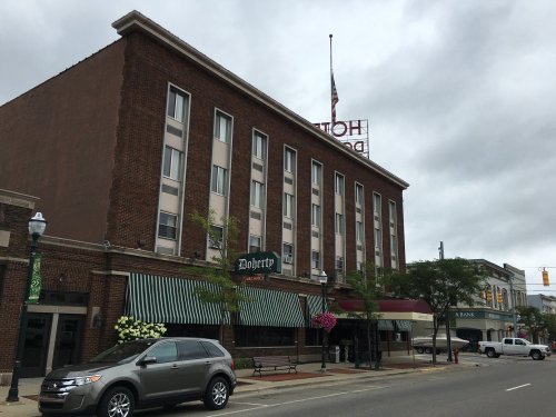 A brick building with a sign reading "Doherty's" and an American flag, set in a small town street under cloudy skies.