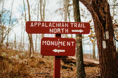 A wooden signpost indicating directions for the Appalachian Trail North and a monument, surrounded by trees.