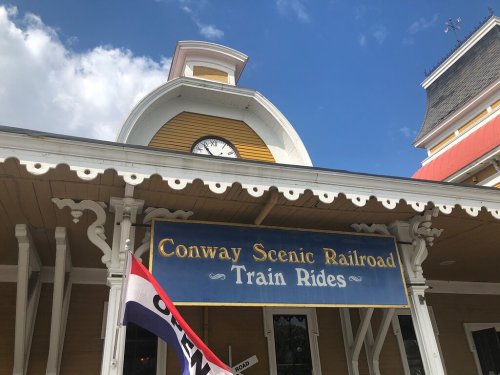 Sign for Conway Scenic Railroad Train Rides, featuring a clock and decorative architecture under a blue sky.