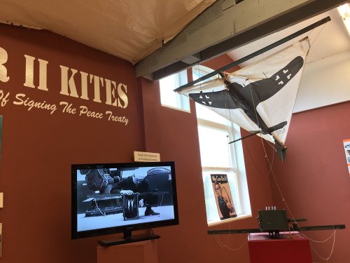 A display featuring a WWII kite hanging from the ceiling, with a TV showing historical footage in the background.
