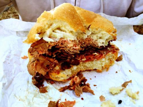 A partially eaten sandwich with layers of beef, topped with coleslaw, resting on crumpled white paper.