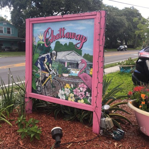 Colorful sign for Chattaway featuring a cyclist and tropical plants, with a pink frame and decorative lights.