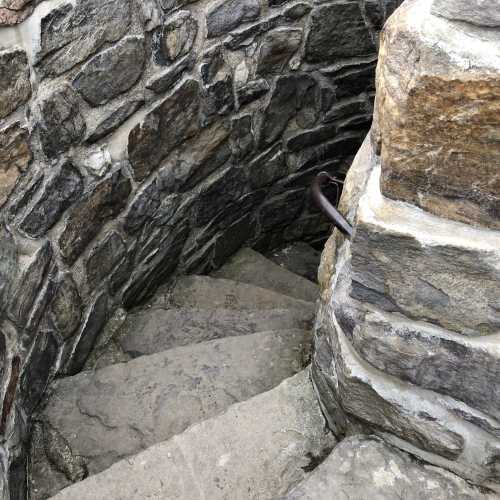 A narrow stone staircase winding down, surrounded by rough stone walls.