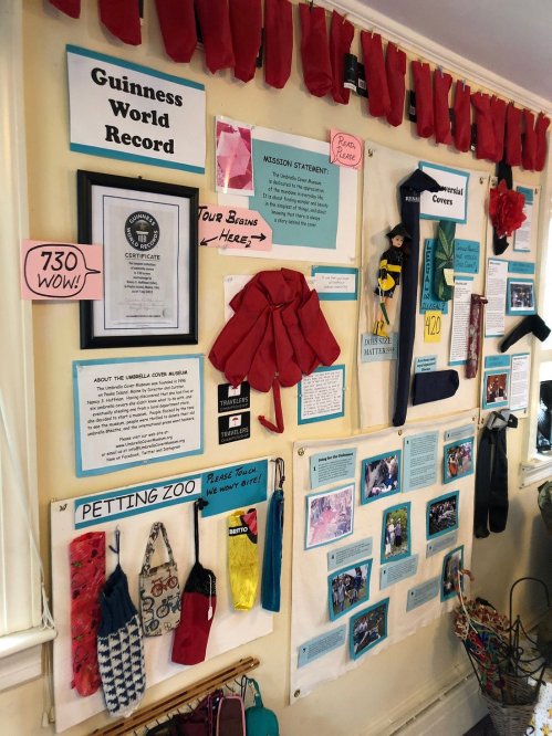 A wall display featuring a Guinness World Record certificate, mission statements, and various colorful umbrella covers.