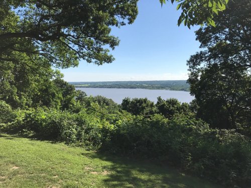 A scenic view of a river surrounded by lush greenery and trees under a clear blue sky.