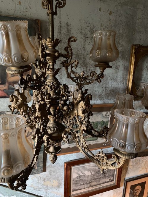 An ornate chandelier with glass shades, surrounded by vintage artwork and a textured wall.