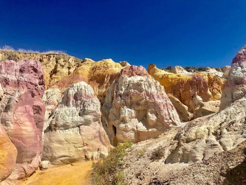 Colorful rock formations in shades of pink, yellow, and white under a clear blue sky.