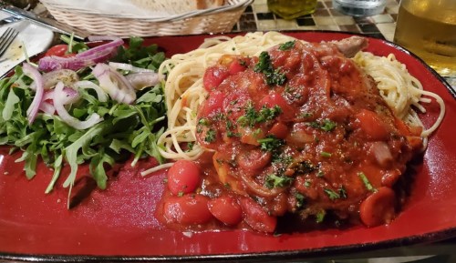 A plate of spaghetti topped with tomato sauce and herbs, served with a side salad of arugula and red onions.