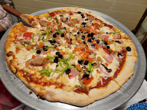 A large pizza topped with cheese, pepperoni, sausage, olives, green peppers, onions, and tomatoes on a metal tray.