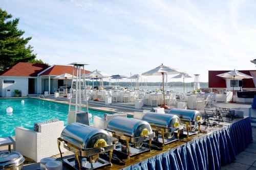 Outdoor event space featuring a pool, dining setup, and catering stations with a scenic waterfront view.