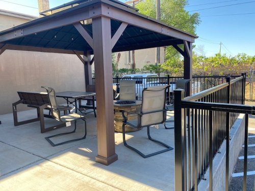 A shaded outdoor seating area with a gazebo, tables, and chairs on a concrete patio.