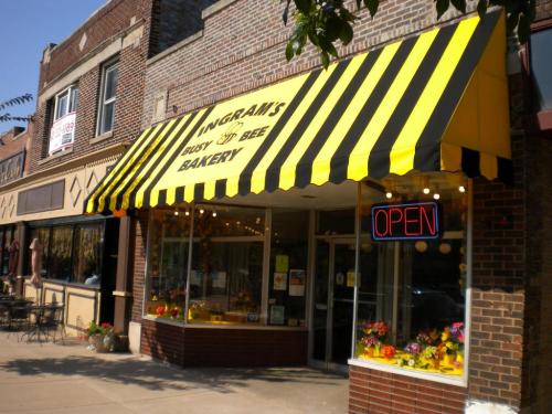 A bakery with a yellow and black striped awning, large windows displaying baked goods, and an "OPEN" sign.