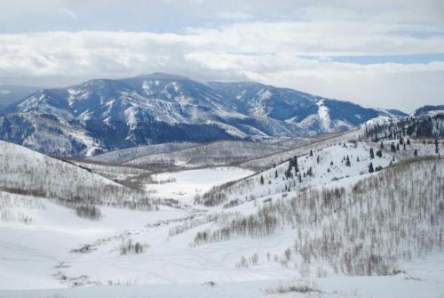 Snow-covered mountains and rolling hills under a cloudy sky, creating a serene winter landscape.