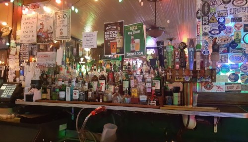A vibrant bar scene with a variety of liquor bottles, colorful lights, and stickers on the walls.