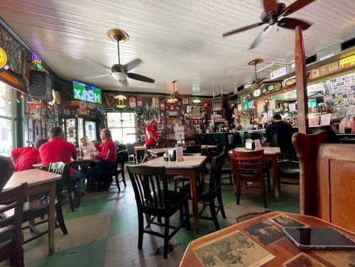 A cozy restaurant interior with wooden tables, fans, and walls adorned with memorabilia. Diners are seated at tables.