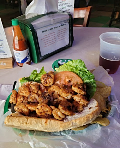A sandwich filled with grilled shrimp, lettuce, and tomato, served with chips and a drink on a table.