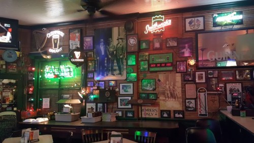 A cozy pub interior with neon signs, framed photos, and a wooden bar, creating a warm, inviting atmosphere.