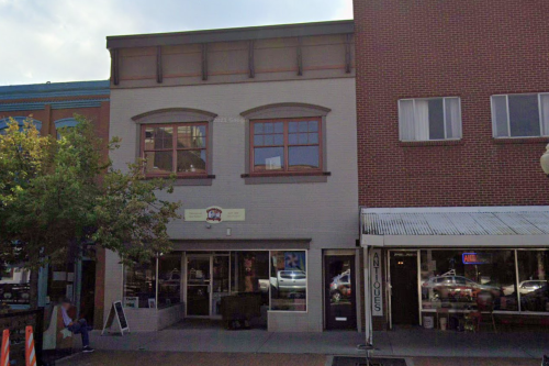 A two-story building with large windows, featuring a storefront and a sign, located on a busy street.