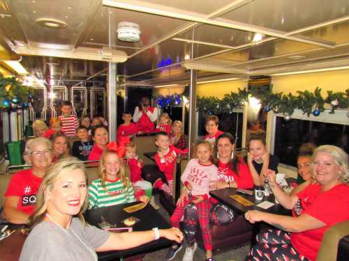 A festive group of adults and children in holiday attire, smiling and seated in a decorated train car.