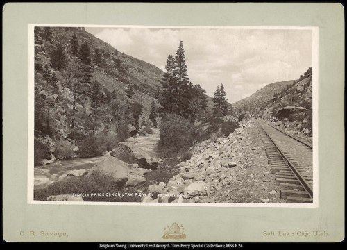 A scenic view of a river and railroad tracks surrounded by mountains and trees in Utah.