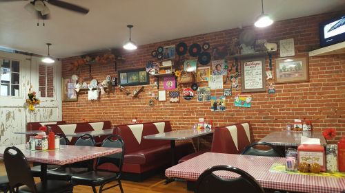 Cozy diner interior with red brick walls, checkered tablecloths, and vintage decor, including records and framed photos.