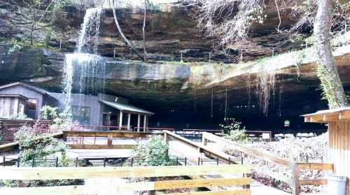 A serene cave interior with a waterfall, wooden structures, and lush greenery surrounding the area.