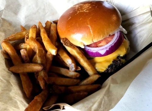 A juicy cheeseburger with tomato and onion, served with a side of crispy golden fries in a paper-lined basket.