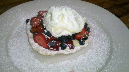 A dessert plate featuring a waffle topped with strawberries, blueberries, whipped cream, and a dusting of powdered sugar.