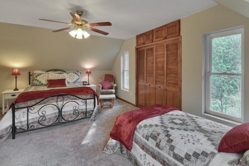 Cozy bedroom with two beds, a ceiling fan, and natural light from windows, featuring warm decor and a closet.