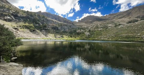 Views of Island Lake, a hidden alpine lake in Nevada, surrounded by mountains and trees under a partly cloudy sky.