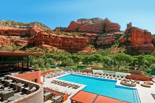 A luxurious pool area surrounded by lush greenery and stunning red rock formations under a clear blue sky.