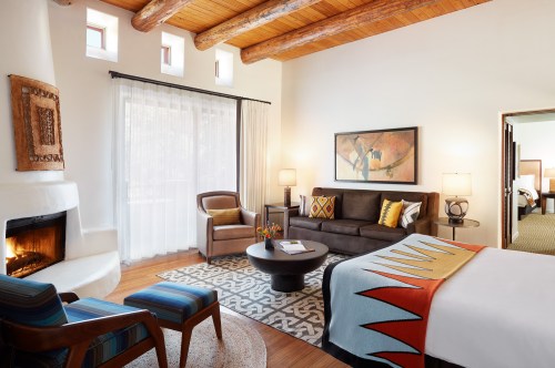 Cozy hotel room featuring a sitting area, fireplace, and colorful decor with wooden beams and large windows.