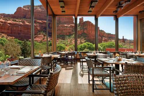 A dining area with wooden tables and chairs, featuring large windows showcasing a scenic view of red rock formations.