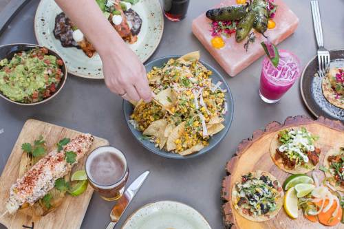 A vibrant spread of Mexican dishes, including nachos, tacos, guacamole, and drinks, on a table.