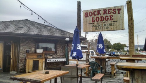 Exterior of Rock Rest Lodge, featuring a wooden sign, outdoor seating, and a rustic stone facade.