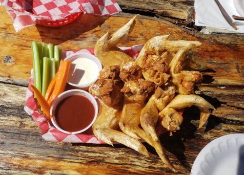 A platter of crispy chicken wings with celery and carrot sticks, served with dipping sauces on a rustic wooden table.