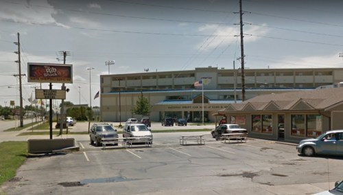 A parking lot with several cars, featuring a restaurant and a large building in the background, likely a sports venue.