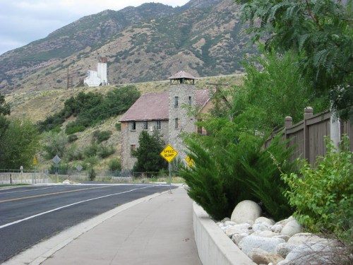 A stone building beside a road, with mountains in the background and a "Speed Limit" sign nearby.