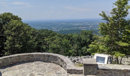 A stone overlook with a panoramic view of green hills and valleys under a clear blue sky.