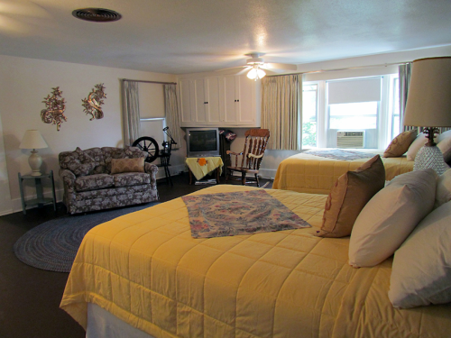 A cozy room with two beds, a sofa, a rocking chair, and a TV, featuring yellow bedding and light-colored decor.