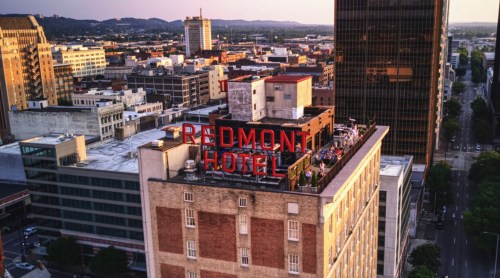 Aerial view of the Redmont Hotel sign atop a building in a city skyline during sunset.